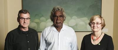 Man in suit holding award, smiling. Background: blurred crowd, stage.