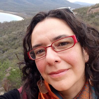 Woman smiling, headshot, dark hair, professional attire, against a blurred background.