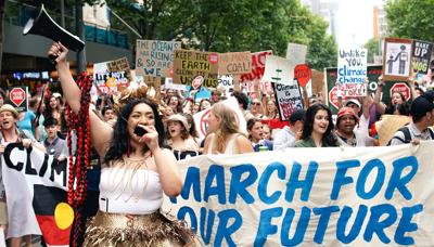 Protest in Melbourne, crowd with signs, buildings in background.