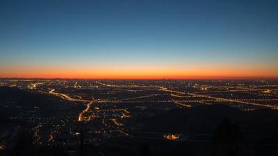 Sunset over city skyline, silhouetted buildings, orange and purple sky.