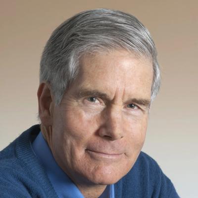 Woman in a white shirt, smiling, holding a phone, standing outdoors with trees in the background.