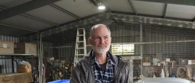 Woman in a hat, smiling, holding a camera, outdoors, trees in background.
