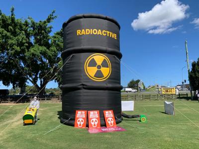 Woman in a blue shirt smiles, holding a baby. Outdoors, trees in background.