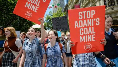 Kids at a rally, holding signs, with a banner in the background.