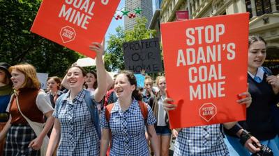 Kids at a rally, holding signs, with a banner in the background.