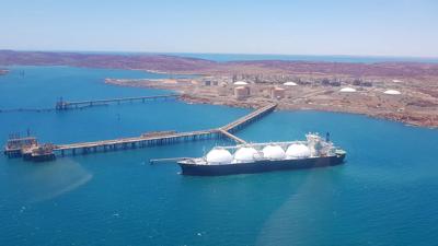 Gas ship being filled up. Large vessel, dockside, hoses connected, blue water, sky.
