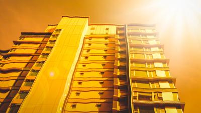 Woman in a white coat, holding a test tube, looking at a microscope in a lab.