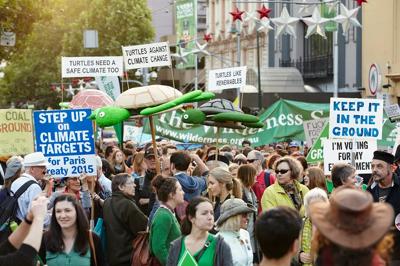 Climate march banner with diverse crowd, holding signs, and a blue sky.