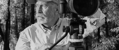 Camera lens, black, close-up, with visible aperture blades and lens elements.