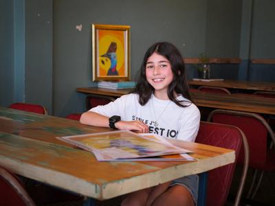 Woman with long hair, smiling, wearing a white top, in front of a blurred background.