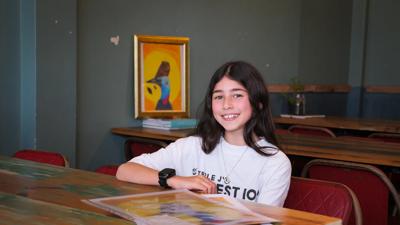 Woman with long hair, smiling, wearing a white top, in front of a blurred background.
