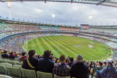 AFL player in action, kicking a football. Stadium background.