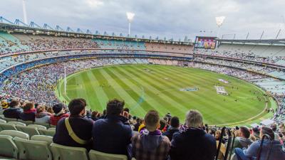 AFL player in action, kicking a football. Stadium background.