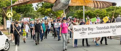 Woman in a white shirt, smiling, holding a camera, outdoors, sunny.