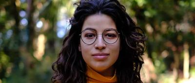 A person in a forest, holding a camera, taking a photo of trees.