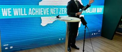 Angus Taylor, a man, in a suit, smiling, outdoors, with a blurred background.