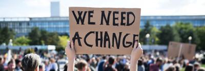 Climate protest sign held up, text visible, crowd blurred background.