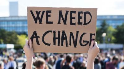 Climate protest sign held up, text visible, crowd blurred background.