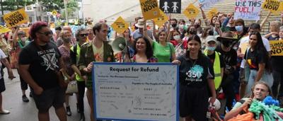 Crowd at a rally, holding signs, with a stage and banners visible.