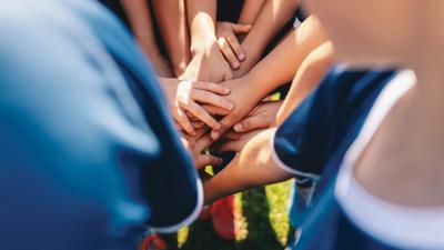 Group of happy children in sports team stacking hands outdoor in a summer day. Children team sports. Boys at sports camp stacking hands before a game. School age children in a team at the grass field