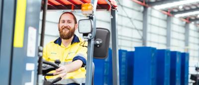 Man in a blue shirt, smiling, outdoors, trees in background, sunny day.