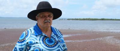 A person in a blue shirt stands near a tree, holding a camera.