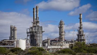 Gas plant infrastructure with pipes, tanks, and industrial structures against a blue sky.