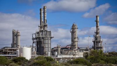 Gas plant infrastructure with pipes, tanks, and industrial structures against a blue sky.