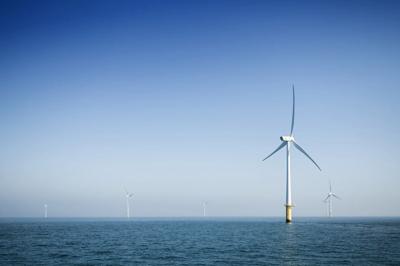 Offshore wind turbines silhouetted against a sunset sky over the ocean.