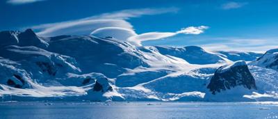 Blue ice landscape, Antarctica. Snow-covered mountains in background, clear sky.