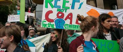 Woman in white coat, holding a clipboard, smiling, looking at camera.