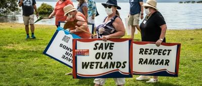 Woman in field, holding camera, smiling. Trees and sky in background.