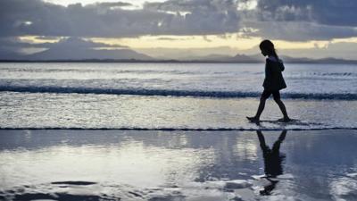 Girl on beach, looking at ocean, sunny day.