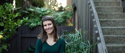 Woman with long hair, smiling, wearing a floral dress, standing outdoors.