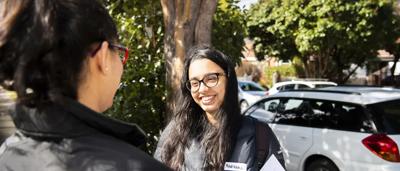 Woman in field, holding camera, smiling. Sunlight, trees in background.