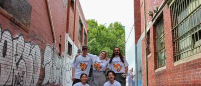 Woman in blue shirt, smiling, holding a phone, standing outdoors with trees.