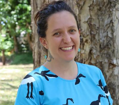 Woman smiling, Queensland Council logo, outdoor setting, daytime.