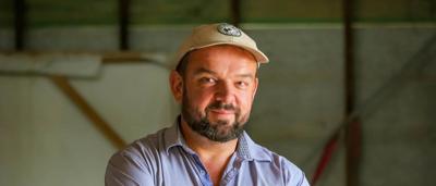 Two men smiling, posing outdoors. One holds a camera. Trees in background.