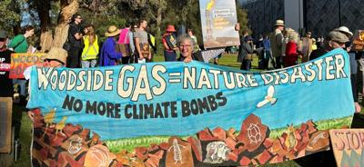 Woodside AGM header image: Text over a photo of people, oil rigs, and a blue sky.