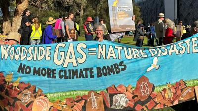Woodside AGM header image: Text over a photo of people, oil rigs, and a blue sky.