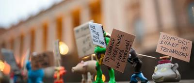 Woman in white coat, holding a plant, smiling. Laboratory setting, bright.