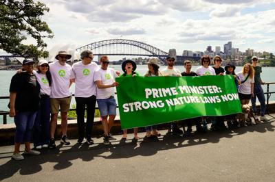 March for Nature 2024: Crowd of people marching, holding signs, trees in background, sunny day.