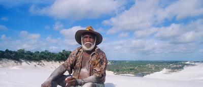 Man in hat, holding a fishing rod, standing on a dock, water in background.