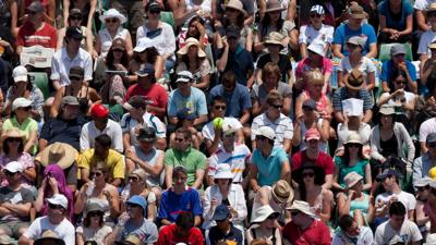 Tennis crowd watching a match, players unseen. Bright sunny day.