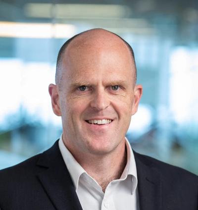 Man in field, holding a camera, looking at a landscape with trees and sky.