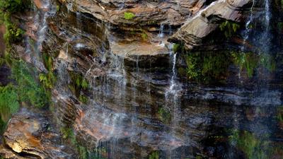 Wentworth Falls waterfall in Blue Mountains, Australia. Lush green foliage surrounds cascading water.