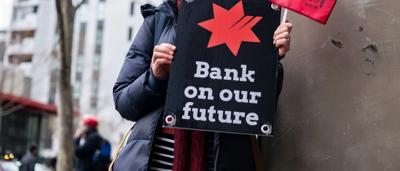 Man in a blue shirt, holding a microphone, speaking at an event with a crowd.