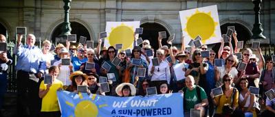 Man in suit, holding a sign, standing in front of a building, text on sign.