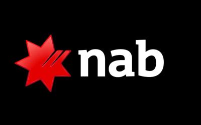 Woman in a white coat, holding a clipboard, smiling, looking at a laptop screen.