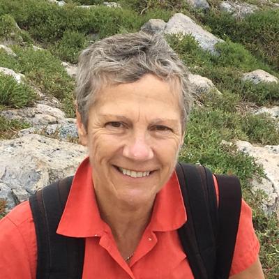 Woman in a white shirt, smiling, looking at the camera, with a blurred background.